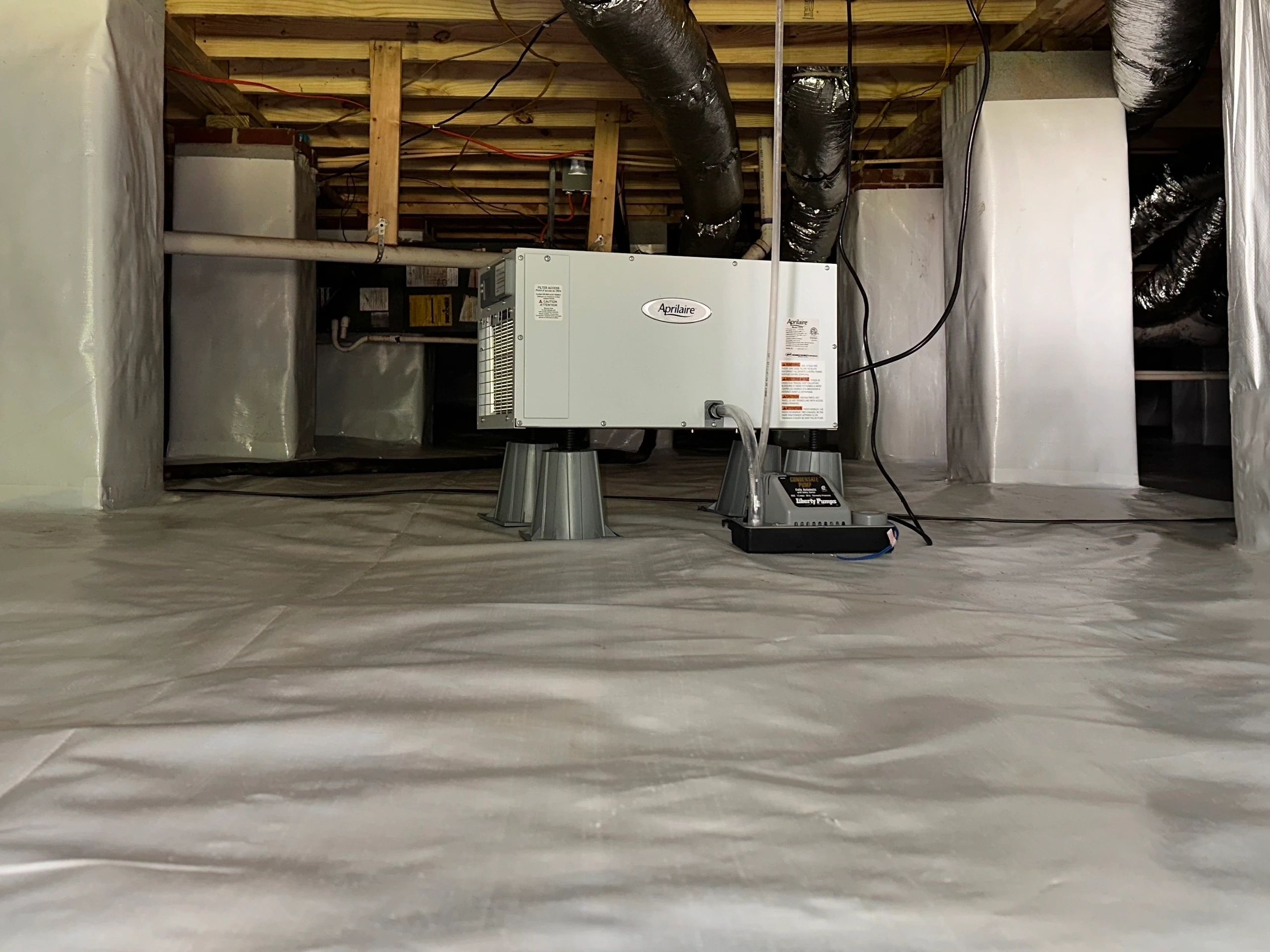 A dehumidifier set on the sealed floor with the ductwork run overhead.
