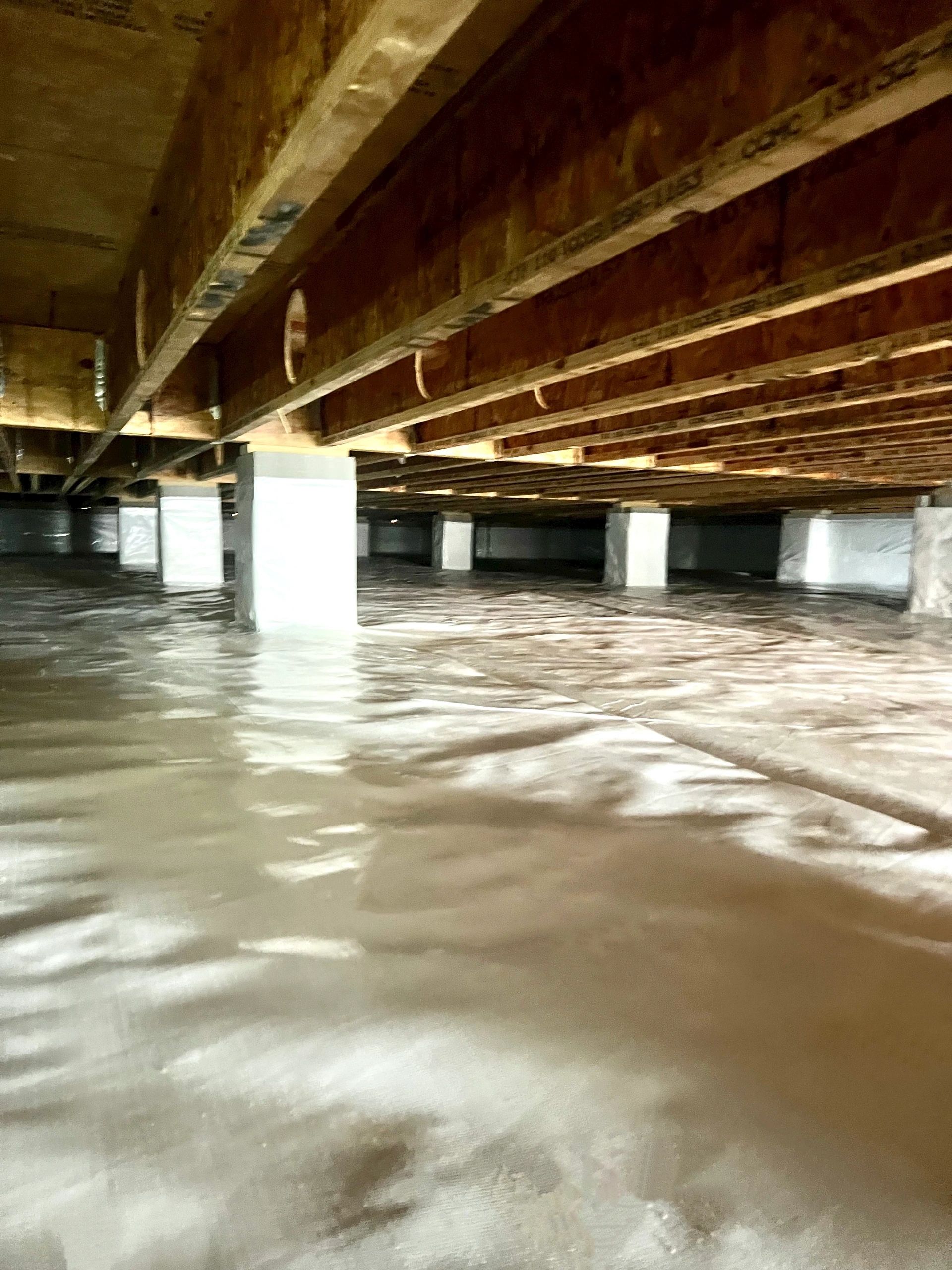 A finished crawl space, the ground and piers sealed under a bright white liner, running away into the dark.