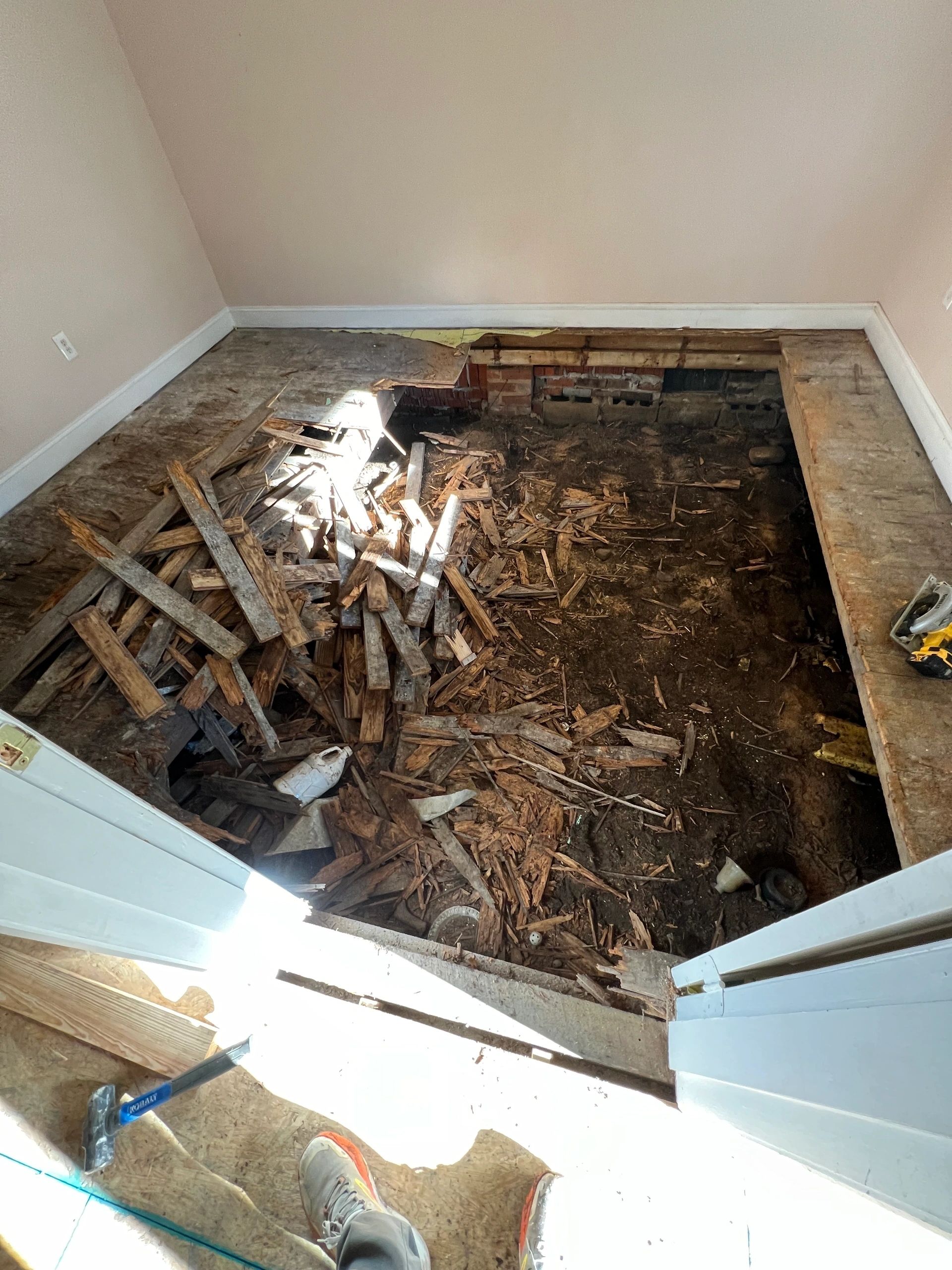 A room with the floor lifted, joists and bare ground open underneath.