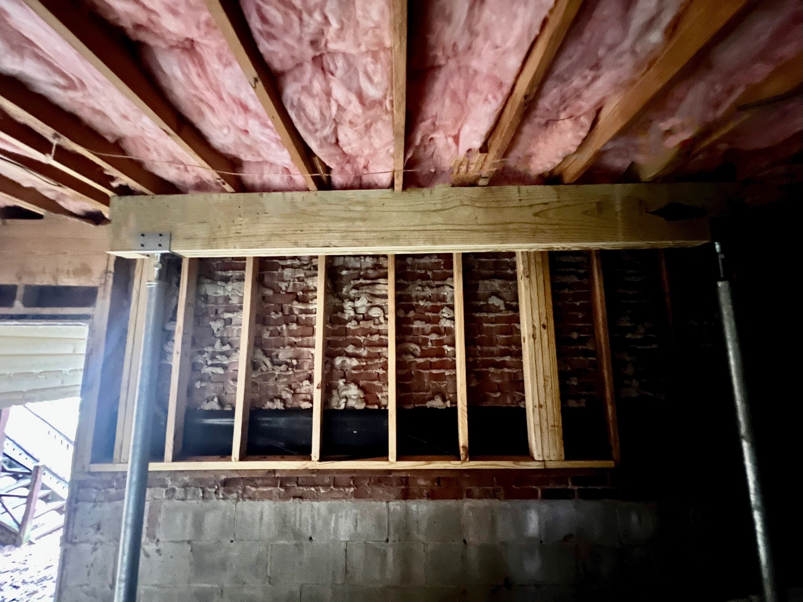 New framing set against the old brick foundation wall, insulation above.